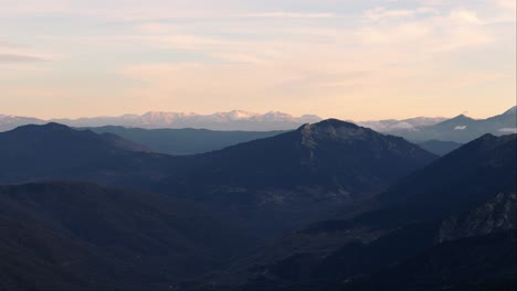 Vista-Aérea-Panorámica-Sobre-Las-Montañas-Del-Valle-Profundo-De-Agrafa-Grecia-A-La-Hora-Azul-Con-Un-Suave-Brillo-Dorado-En-El-Horizonte