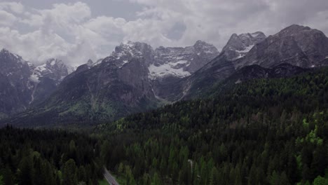 Aerial-green-pine-trees-with-snowy-rocky-mountain-peaks,-Dolomites