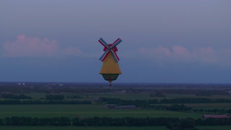 Aerial-view-of-colorful-hot-air-balloon-in-windmill-shape-at-sunset,-Netherlands