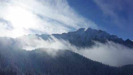 Misty-Bucegi-Mountains-with-sunlit-peaks-and-forested-slopes,-serene-nature-scene