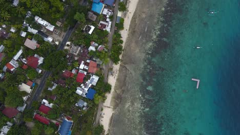Aerial-Drone-Rotates-Above-Tropical-Beach-Travel-Coastline-Turquoise-Sea-Water,-Roofs-Houses-and-Resorts-around-Tropical-Greenery-of-Oslob-Celu-Island-Philipines