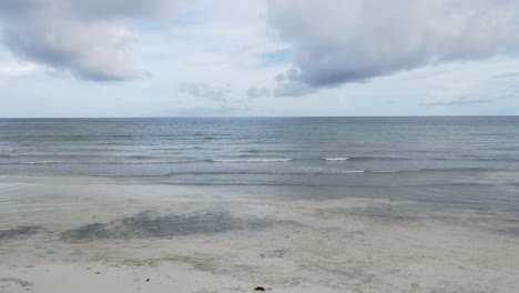 Drohne-Fliegt-Schnell-über-Weißem-Sand-Und-Meereswelleneingang-Mit-Panoramablick-Auf-Die-Skyline-Aus-Der-Vogelperspektive