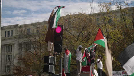 Ein-Arabischer-Mann,-Der-Bei-Einer-Pro-palästinensischen-Demonstration-Mit-Einer-Großen-Menschenmenge-Von-Demonstranten-Eine-Palästinensische-Flagge-Auf-Einer-Straßenlaterne-Schwenkt