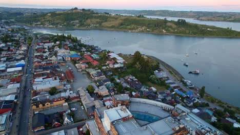 View-from-above-establishing-Castro-Chiloe,-at-dawn-with-fishing-boats-on-its-coast,-Chile