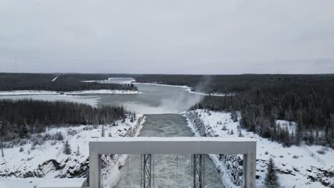 Slow-Reveal-Drone-Shot-Snow-Covered-Road-with-Rushing-Water-Notigi-Hydroelectric-Dam-in-the-Arctic