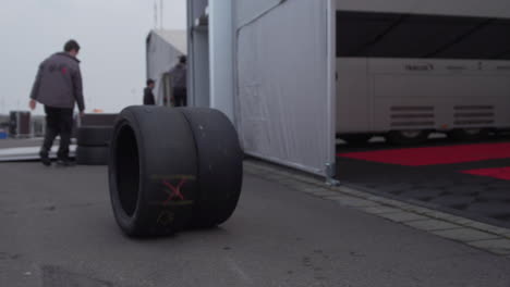 Mechanic-rolling-tires-to-colleague-for-storage,-racing-paddock