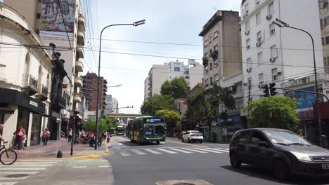 Autobuses,-Transporte-Público-De-La-Ciudad-De-Buenos-Aires-Por-La-Avenida-Rivadavia,-Peatones,-Edificios-Y-Arquitectura-Urbana-Del-Barrio-De-Flores,-Argentina