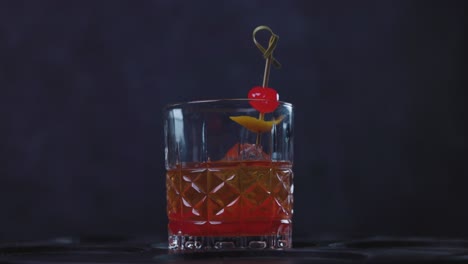 Old-Fashioned-cocktail-drink-chilean-version-with-bourbon-whiskey,-sugar,-ice,-bitter-dashes,-maraschino-cherry-in-dark-background-and-selective-focus