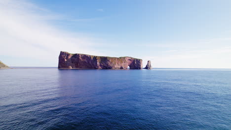 Drone-view-centered-on-Percé-Rock-above-the-Saint-Lawrence-River,-receding-during-a-sunny-day