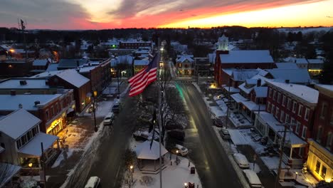 Twilight-over-snowy-main-street-with-American-flag,-gazebo,-and-historic-buildings