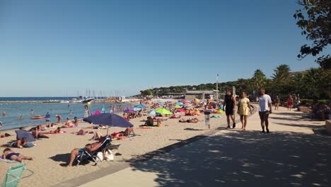 Toma-En-Cámara-Lenta-De-Gente-Caminando-Y-Tumbada-En-La-Playa-En-Antibes,-Francia.