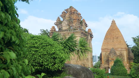 Dolly-Revela-Las-Torres-Po-Nagar-Cham-Desde-Detrás-De-Arbustos-Tropicales-En-El-Antiguo-Jardín-Del-Templo-Hindú---Cámara-Lenta