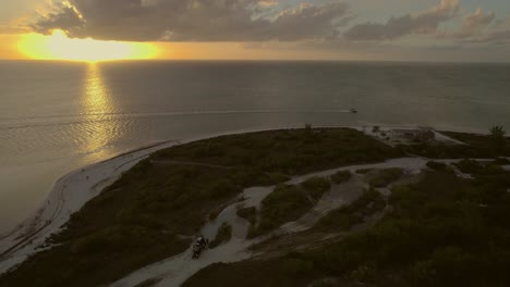 Vista-Aérea-Cinematográfica-De-Una-Puesta-De-Sol-Sobre-Una-Playa,-Con-Un-Barco-A-Toda-Velocidad.