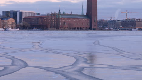 Revelación-Aérea-Del-Atardecer-Del-Ayuntamiento-De-Estocolmo-Sobre-Riddarfjärden-Congelado,-Suecia