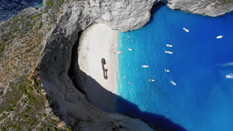 Aerial:-Rising-top-down-view-of-Navagio-beach-in-Zakynthos-island,-Greece-during-summer