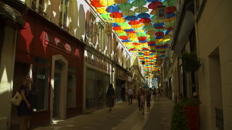 Los-Peatones-Caminando-Bajo-Un-Mar-De-Sombrillas-En-Una-Estrecha-Calle-Comercial,-Estática