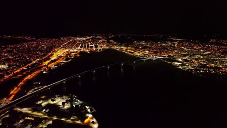 Night-view-of-Sundsvall-Bridge-in-Sweden,-glowing-city-lights,-aerial-perspective