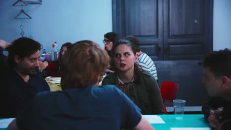 Chica-Con-Cola-De-Caballo-Llevando-A-Un-Hombre-Sentado-Alrededor-De-Una-Mesa-En-Un-Salón-De-Clases.