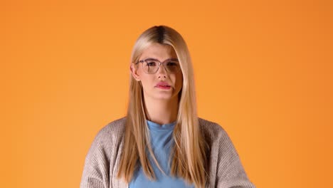 Una-Joven-Rubia-Llora-Tristemente-Mirando-La-Cámara-Y-Preguntándose,-Foto-Cromática-De-Estudio,-Gafas-Y-Lápiz-Labial-Rojo,-Inteligente