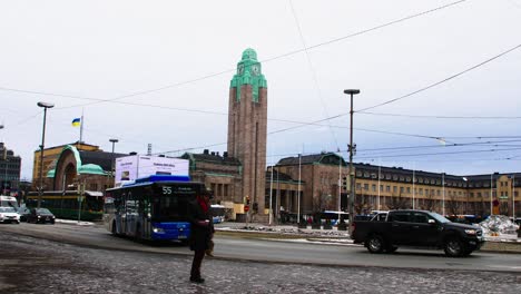 Winter-day-at-Helsinki-Central-Station-with-bustling-traffic-and-pedestrians,-tram-in-motion,-cloudy-sky