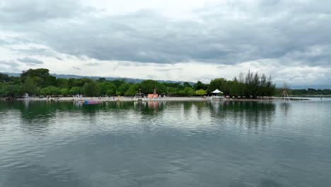 Calm-waters-of-Pantai-Batuhoda-at-Lake-Toba-with-cloudy-skies-and-lush-greenery,-Sumatra,-Indonesia