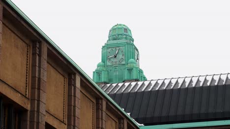 Turquoise-clock-tower-peeking-over-railway-station,-Helsinki,-overcast-day