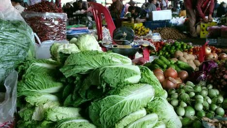 Una-Vista-De-Primer-Plano-Muestra-Una-Variedad-De-Vegetales-De-Hojas-Verdes-Y-Vibrantes-Vegetales-Sin-Hojas,-Con-Individuos-No-Identificables-Visibles-En-El-Fondo