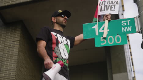 Ein-Arabischer-Mann-In-Einem-Free-Palestine-Shirt,-Der-Beim-Marsch-Auf-Washington-Ein-Waffenstillstandsschild-Auf-Einem-Straßenschild-Hält