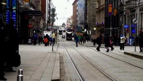 Bustling-Helsinki-street-scene-with-pedestrians-and-tram,-daytime,-urban-atmosphere,-overcast-sky