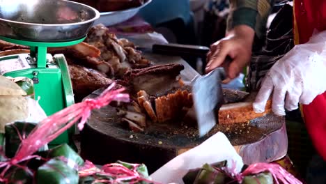 A-person's-hand,-absent-of-any-facial-features,-is-seen-slicing-crispy-pork-with-a-flat-Chinese-knife-on-a-wooden-cutting-board