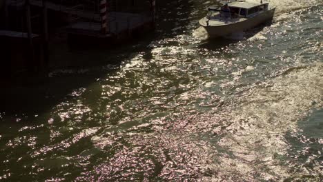 Taxi-boat-on-the-water-of-Canal-Grande-in-Venice,-Italy,-is-cruising-under-a-bridge-in-the-morning-sunlight