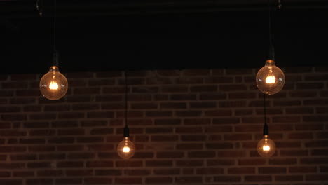 Vintage-Glühbirnen-Von-Edison-Hängen-über-Einer-Dunklen,-Nackten-Ziegelwand-In-Einem-Stilvollen,-Modernen-Zimmer