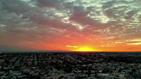 Puesta-De-Sol-Que-Proyecta-Tonos-Vibrantes-Sobre-Un-Extenso-Paisaje-Urbano,-Nubes-Pintando-Un-Cielo-Espectacular,-Vista-Aérea