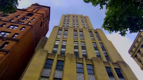 El-Edificio-Icónico-Que-Se-Asemeja-Al-Daily-Planet-Del-Cómic-De-Superman-Fue-Construido-Durante-La-Era-Del-Cubismo-En-Montreal,-Capturando-Desde-Un-ángulo-Bajo-La-Vista-De-Los-Gusanos,-Las-Nubes-Que-Cambian-El-Día-De-Verano,-Los-Ciclistas-Pasan-Rápidamente.