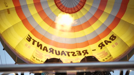 Looking-up-at-propane-gas-flames-filling-hot-air-balloon-to-inflate-colourful-canopy