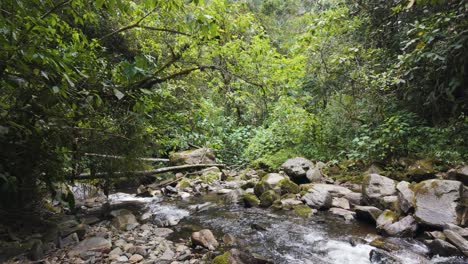 Pan-across-tropical-river-running-through-flooded-boulder-strewn-valley-grounds-in-Cocora-Valley-Colombia