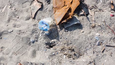 Close-up-of-crab-cleaning-up-sand-from-hole-home-on-beach-surrounded-by-plastic-rubbish-pollution-washed-ashore-from-ocean-on-tropical-island-destination