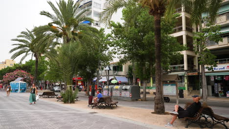 Tourists-strolling-along-Mallorca-waterfront-promenade-shops-with-palm-trees-and-bench-seating
