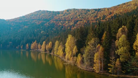 Autumn-colors-line-Lake-Sfanta-Ana-in-Harghita,-serene-water-reflecting-trees