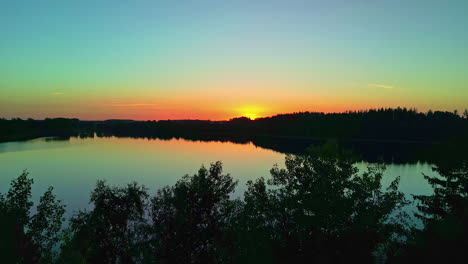 Wunderschöner-Sonnenuntergang-über-Einem-Ruhigen-See-Mit-Baumsilhouette-Aus-Einer-Drohnenaufnahme-Mit-Dolly