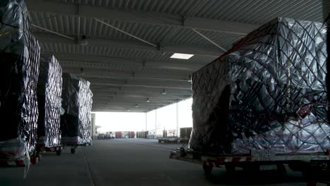 Dark-warehouse-interior-with-rows-of-pallets-wrapped-in-black-plastic,-potential-for-storage-or-shipping-concepts