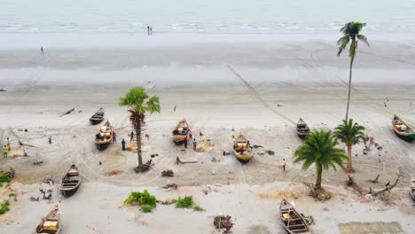 Aerial-view-of-fishermen-around-wooden-boats-on-a-palm-fringed-beach-in-Bangladesh