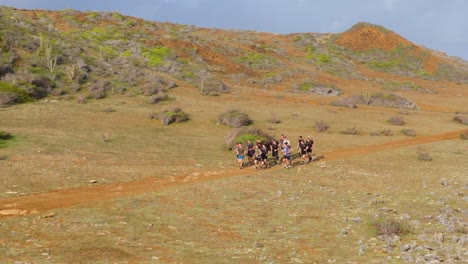 Un-Grupo-De-Hombres-Corren-Juntos-En-Paquete-A-Través-De-Un-Camino-De-Tierra-árido-Y-Seco-Con-Arbustos-Doblados-Por-El-Viento-De-Krumholz