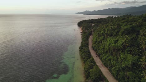 Scenic-aerial-drone-shot-of-lush,-tropical-island-and-clear-ocean-waters-with-motorcycle-driving-on-coastal-road