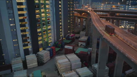 Truck-Transporting-Goods,-Elevated-Logistics-Road,-on-top-of-Hong-Kong-Container-Shipping-Yard,-After-Dark,-Wide-Angle-Aerial-Follow-Shot,-Cinematic-Anamorphic-Look