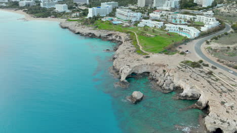 Rocky-coastline-of-Ayia-Napa-with-rocks-underwater-and-hotel-resort-in-background