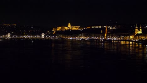 Vista-Del-Centro-De-La-Ciudad-De-Budapest-Con-El-Castillo-De-Buda-Y-El-Río-Danubio-Por-La-Noche,-Arquitectura-Gótica,-Reflejos-De-Luz,-Toma-Muy-Distante