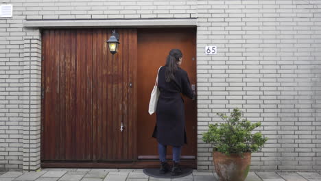 Mujer-Joven-Que-Cierra-La-Puerta-De-Una-Casa-Moderna,-Alejándose-Con-Un-Bolso,-Amplia