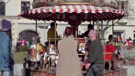 Ein-Kleines-Karussell,-Auf-Dem-Kinder-Fahren-Und-Ihre-Eltern-Während-Eines-Karnevalsfestes-In-Der-Innenstadt-Von-Brixen,-Südtirol,-Italien-Zuschauen