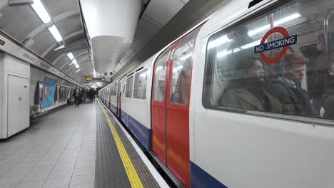 Bakerloo-Line-Zug-Fährt-Am-Bahnsteig-Der-Oxford-Street-Ab,-Pendler-Laufen-Hinter-Der-Gelben-Linie-Her